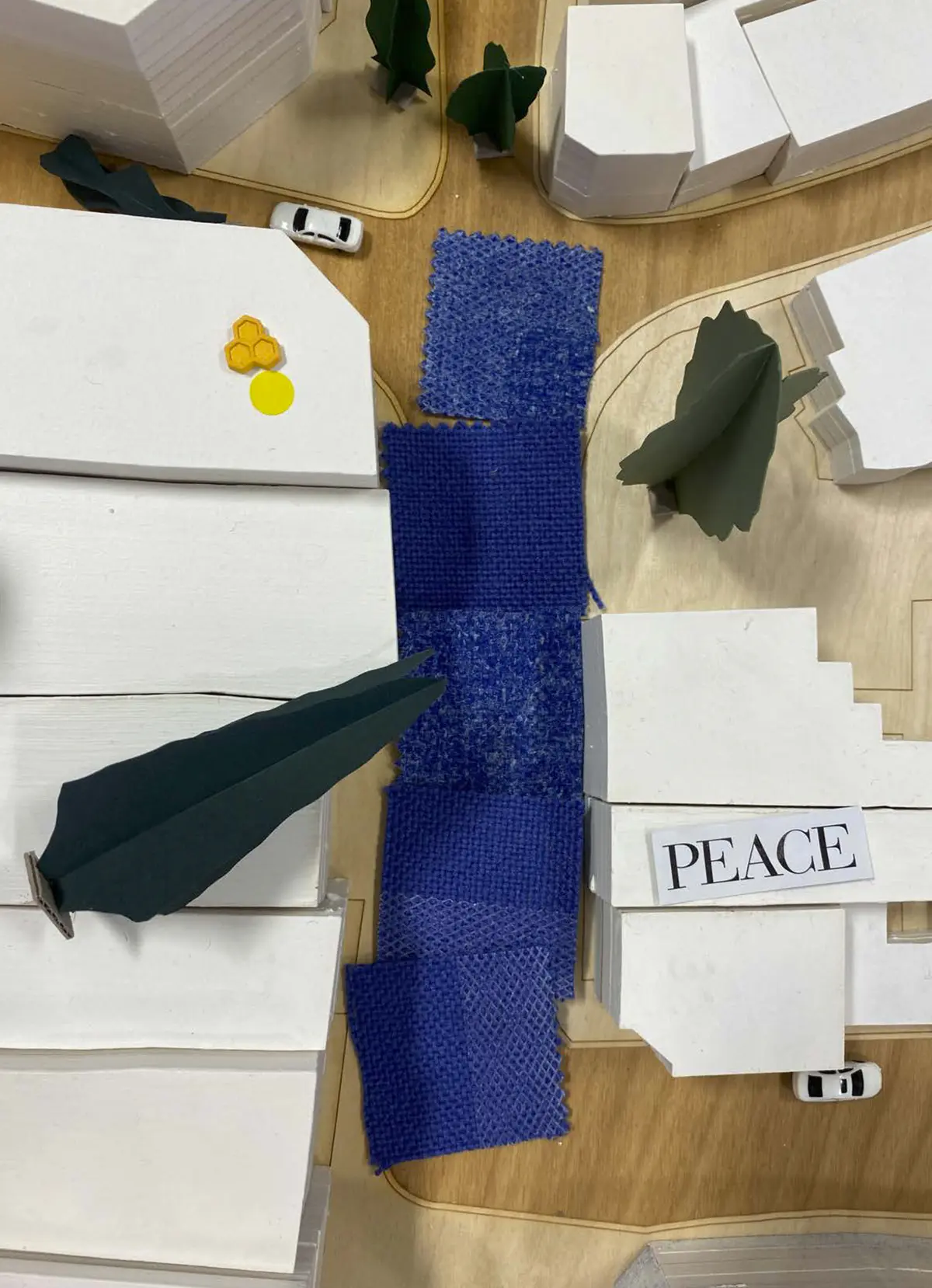 Looking to be the centrepiece of our exhibition, we proposed to create a site model of Dudley Highstreet at 1:200 scale with buildings modelled in a simple form. Local residents and visitors to the exhibition are then invited to decorate a chosen building to how they would envision it sat within the context of a greener Highstreet. We want to tie in our themes of biodiversity and materials by proposing that buildings can, and do, have the potential to be a lot healthier, sustainable, and interactive on the street. This site model also helps gain vital public opinions on the Highstreet and prompts discussion of areas most in need of attention.

To ensure that the model is utilising the MDF to the most efficient standard possible. First, the centres of the massing blocks have been hollowed out. This allows a reduction in materials used as other buildings can be cut in the centres of the model. Then the top is finished with a solid piece.
The waste material is placed into the recycling rack where other students can reuse it; otherwise, if the material left cannot be used for another project, it is recycled correctly by the university.

The model spanned just over 3.4m long and over 50cm wide. With the majority being cut from scrap woods that would fit the jigsaw of the shape, we were able to drastically cut down on waste. We also got some small benches and bee hives printed from recycled plastics, and used dried flowers as trees to represent the green spaces. Ultimately, the model seemed like a huge success, and really helped portray our ideas about Dudley High Street to those who came by. Everyone from Dudley who saw the model knew that it was the High Street, and interacted well with it. The size did make it difficult to move, especially to carry to the site, but it sat nicely in the centre of the the room and really drew people in to interact with it.

The model brought people in from outside to play with, write on, interact with. It became a spectacle for the public to come in and see what was happening and offer their ideas about what could be done.

The event was a success. Many people from the public (those who heard about the event, and those who just happened across it on the day) came in to interact with the model, which sat as the centre piece in the room. Kids liked to play with the pieces while the adults talked about things that could come from actions to help the High Street, not just leave it as is.

SOME OF THE KEY IDEAS WERE:
- The Shops need to be inviting for everyone. It’s no good having these places to go if people would rather take a bus to the next town.
- Just putting up boards across the windows is awful. Paint, Posters, Graffiti: Anything that actually makes the High Street look still alive is better than just wooden boards.
- More Green is needed. While it is obvious that there is a lack of Trees, many people wanted to push for these small bushes or planting spaces that could easily be implemented across the street.
- Spaces for public events or for people to at least gather at. While there is the Market and Fountain, it is not enough for the people of Dudley.
- Something needs to be done about the cars on the High Street. Some were Pro-Removal of all Cars, while some just wanted to limit when they could access the High Street.

Following the exhibition we created a series of drawings with our own interpretation of Sarah Wigglesworth ‘The Dining Table’ drawing. The drawings are a perfect representation of the our interactive model at the ERA Environmental Exhibition and Event. Showing the interaction the public had with the model, as well as the conversations that were held around the model. - Table 3.png